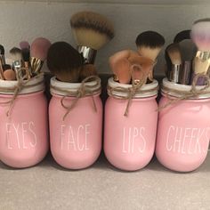 pink jars with makeup brushes in them that say eyes, lips, cheeks