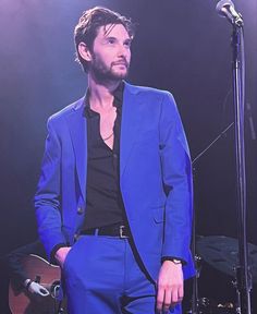 a man in a blue suit and black shirt standing next to a microphone on stage