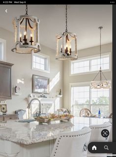 two chandeliers hanging from the ceiling in a kitchen with marble counter tops and white chairs