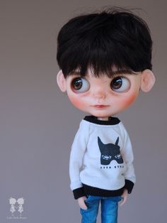 a close up of a doll wearing a sweater and jeans with an animal on it