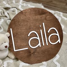 a teddy bear sitting next to a wooden sign that says laia