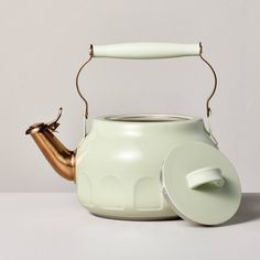 a white teapot with a gold handle and lid on a grey surface, sitting next to a silver kettle