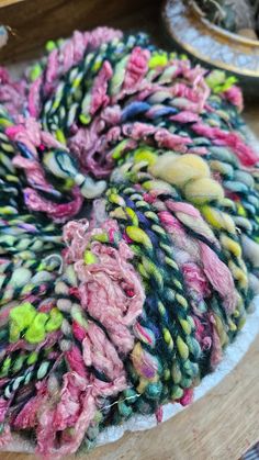 a pile of colorful yarn sitting on top of a wooden table next to a plate