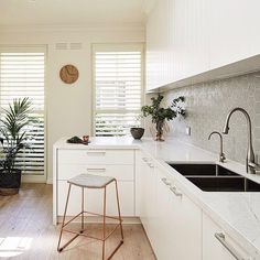 a kitchen with white cabinets and counter tops next to a window covered in shutters