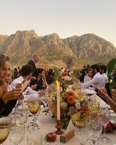 a group of people sitting at a table with wine glasses and plates in front of mountains