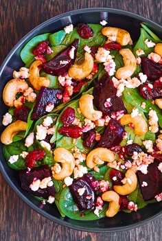 a salad with beets, nuts and spinach leaves in a black bowl on a wooden table