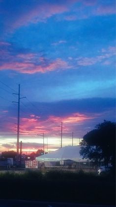 the sun is setting over an industrial area with power lines and telephone poles in the foreground