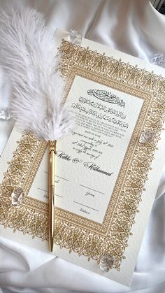 a wedding card with a feather on top of it next to a pen and paper