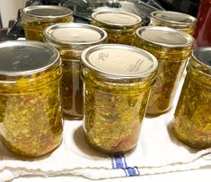 several jars filled with pickles sitting on top of a white table cloth next to an oven