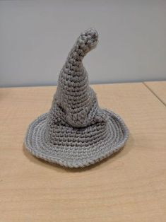 a crocheted gray hat sitting on top of a wooden table next to a wall