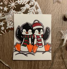 two penguins wearing hats and scarfs on top of a table next to christmas decorations