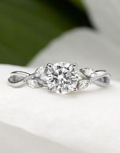 a white gold engagement ring with two diamonds on it's side, sitting on top of a flower