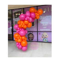 an orange and pink balloon arch in front of a storefront with posters on the windows