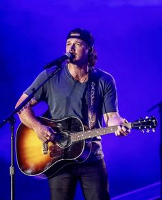 a man holding a guitar while standing in front of a microphone on top of a stage