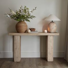 a wooden table with two vases and a lamp on it next to a wall