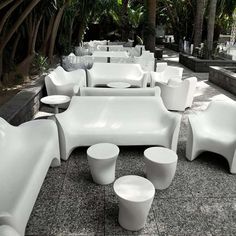 an outdoor seating area with white chairs and stools on the ground next to palm trees