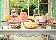 a table topped with lots of cakes and desserts next to a large glass window