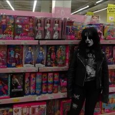 a woman standing in front of a shelf filled with barbie dolls