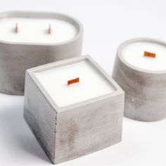 three cement square candles sitting next to each other on a white surface with orange sticks sticking out of them