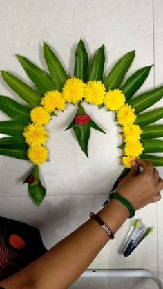 a woman is making a flower wreath with yellow flowers and green leaves on the wall