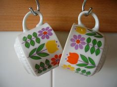 two mugs with flowers painted on them hanging from hooks