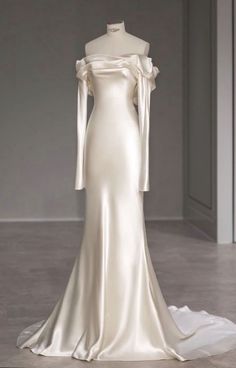 a white wedding dress with long sleeves and an off the shoulder neckline, on display