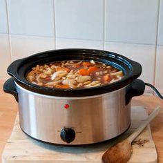 a crock pot filled with soup sitting on top of a wooden cutting board