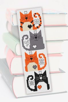 a cross stitch bookmark with cats and kittens on it, sitting next to some books