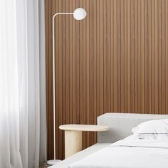 a white bed sitting next to a wooden wall with a lamp on top of it