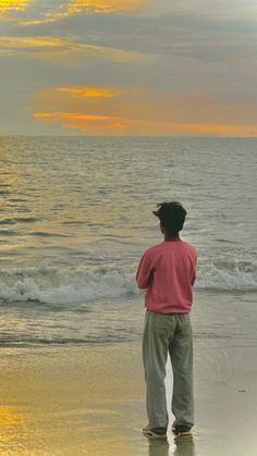 a man standing on top of a beach next to the ocean under a cloudy sky