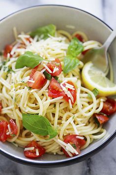 a close up of a bowl of pasta with tomatoes and spinach leaves on the side