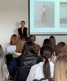 a woman standing in front of a group of people while giving a presentation on a projector screen