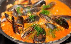 a pan filled with mussels and sauce on top of a stove