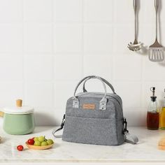 a gray lunch bag sitting on top of a kitchen counter next to utensils