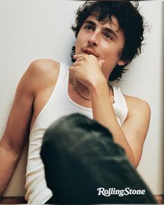 a young man leaning against a wall with his hand on his chin