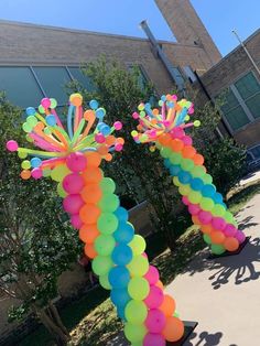 an arch made out of balloons in front of a building with trees and bushes behind it