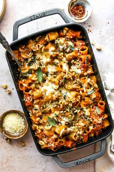 a casserole dish filled with pasta, cheese and vegetables on a white table