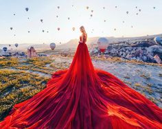 a woman in a red dress standing on top of a hill with hot air balloons