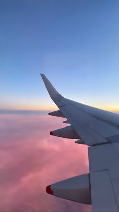 the wing of an airplane as it flies through the sky with pink clouds in the background