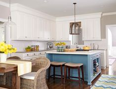 a kitchen with white cabinets, blue island and yellow flowers in vases on the counter