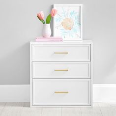 a white chest of drawers with pink flowers on top and an art print above it