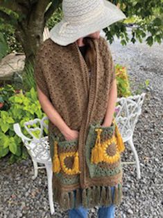 a woman wearing a hat and scarf standing in front of a tree with sunflowers on it