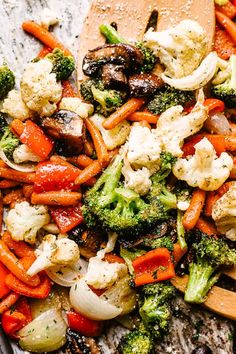 broccoli, cauliflower and carrots are mixed together on a wooden spoon