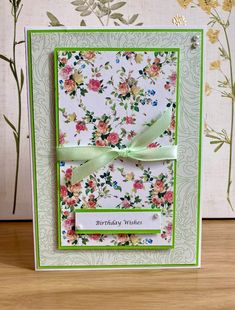 a birthday card with flowers on it and a ribbon around the edge, sitting on a table