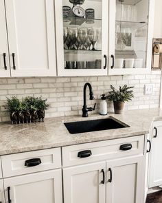 a kitchen with white cupboards and marble counter tops, black faucet handles