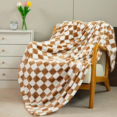 a brown and white checkered blanket sitting on top of a chair next to a vase with flowers