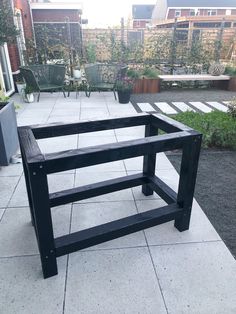 a black bench sitting on top of a cement floor next to a planter filled with potted plants