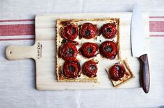 a cutting board topped with slices of bread covered in red peppers and sauces next to a knife