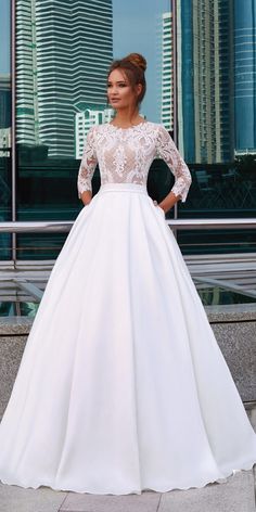 a woman standing in front of a window wearing a white dress with long sleeves and lace detailing