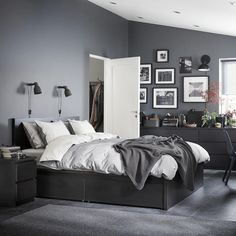 a bedroom with gray walls and white bedding, black furniture and pictures on the wall